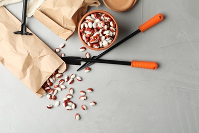 Photo of Paper bag with raw beans and gardening tools on grey table, flat lay. Vegetable seeds