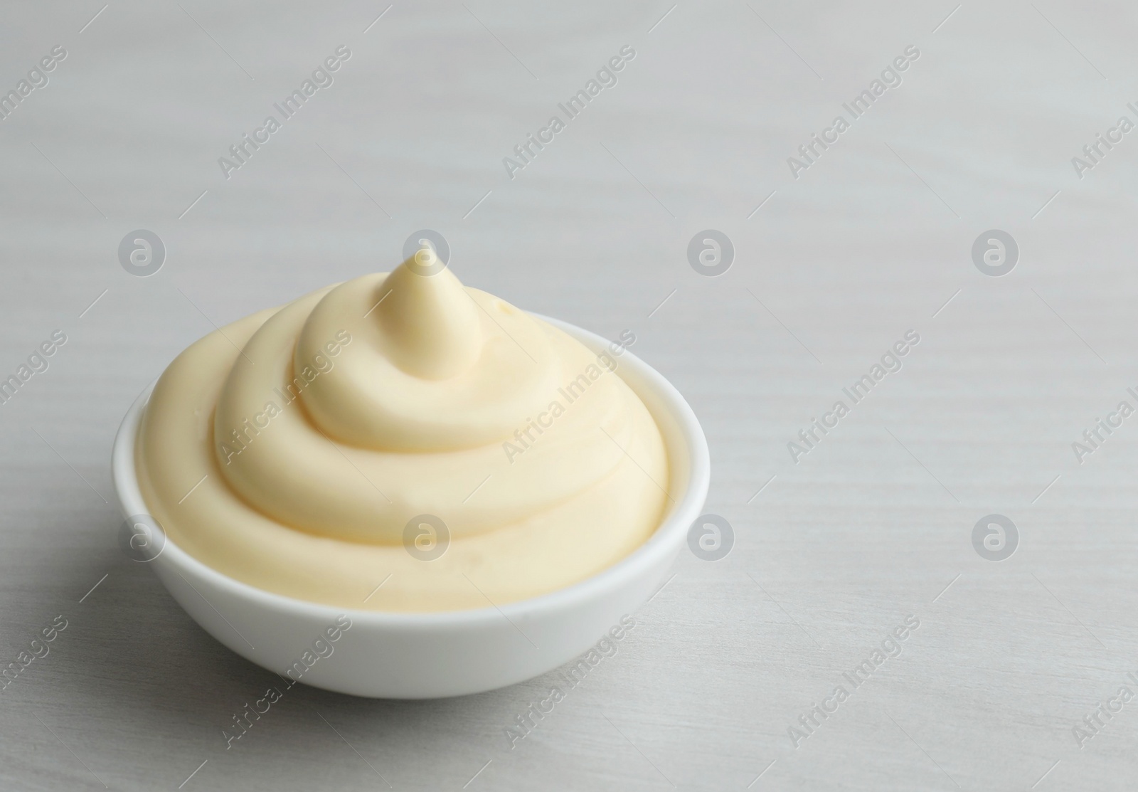 Photo of Tasty mayonnaise sauce in bowl on light wooden table, closeup. Space for text