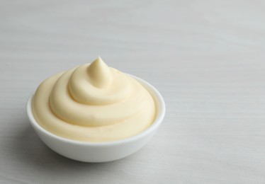 Photo of Tasty mayonnaise sauce in bowl on light wooden table, closeup. Space for text