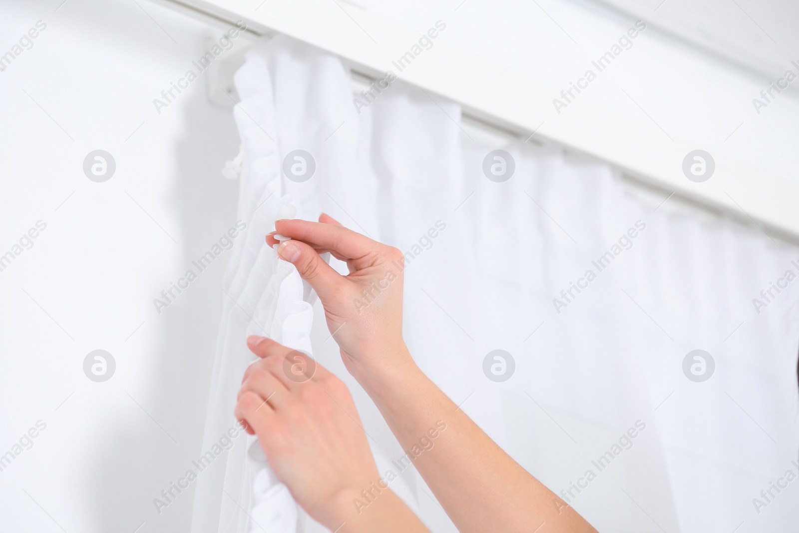 Photo of Young woman hanging window curtain in room, closeup