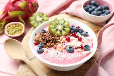 Photo of Tasty smoothie bowl with fresh kiwi fruit, berries and granola on pink wooden table, closeup