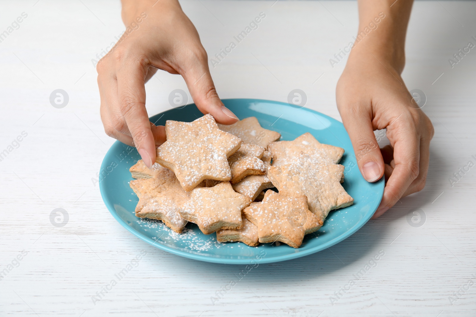 Photo of Woman taking tasty homemade Christmas cookie from plate on table