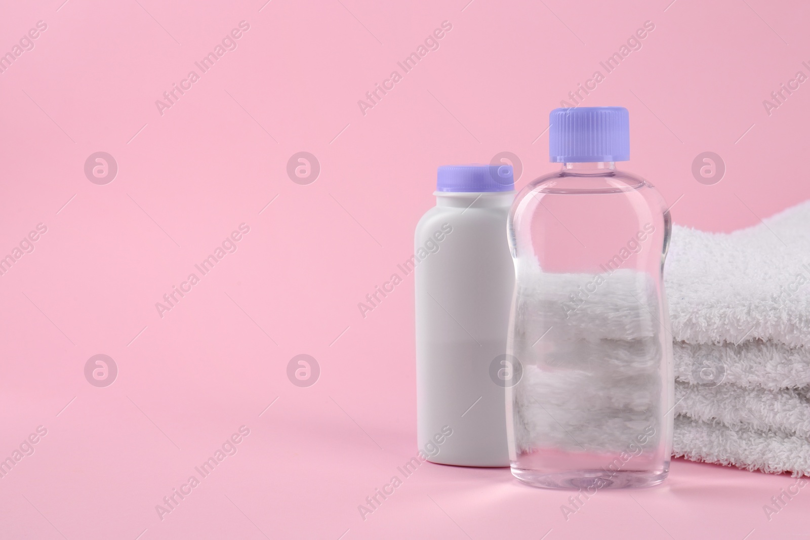 Photo of Bottles with baby oil and powder near soft towel on pink background, space for text