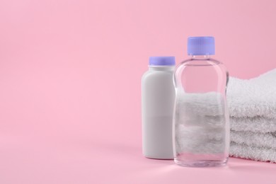 Photo of Bottles with baby oil and powder near soft towel on pink background, space for text