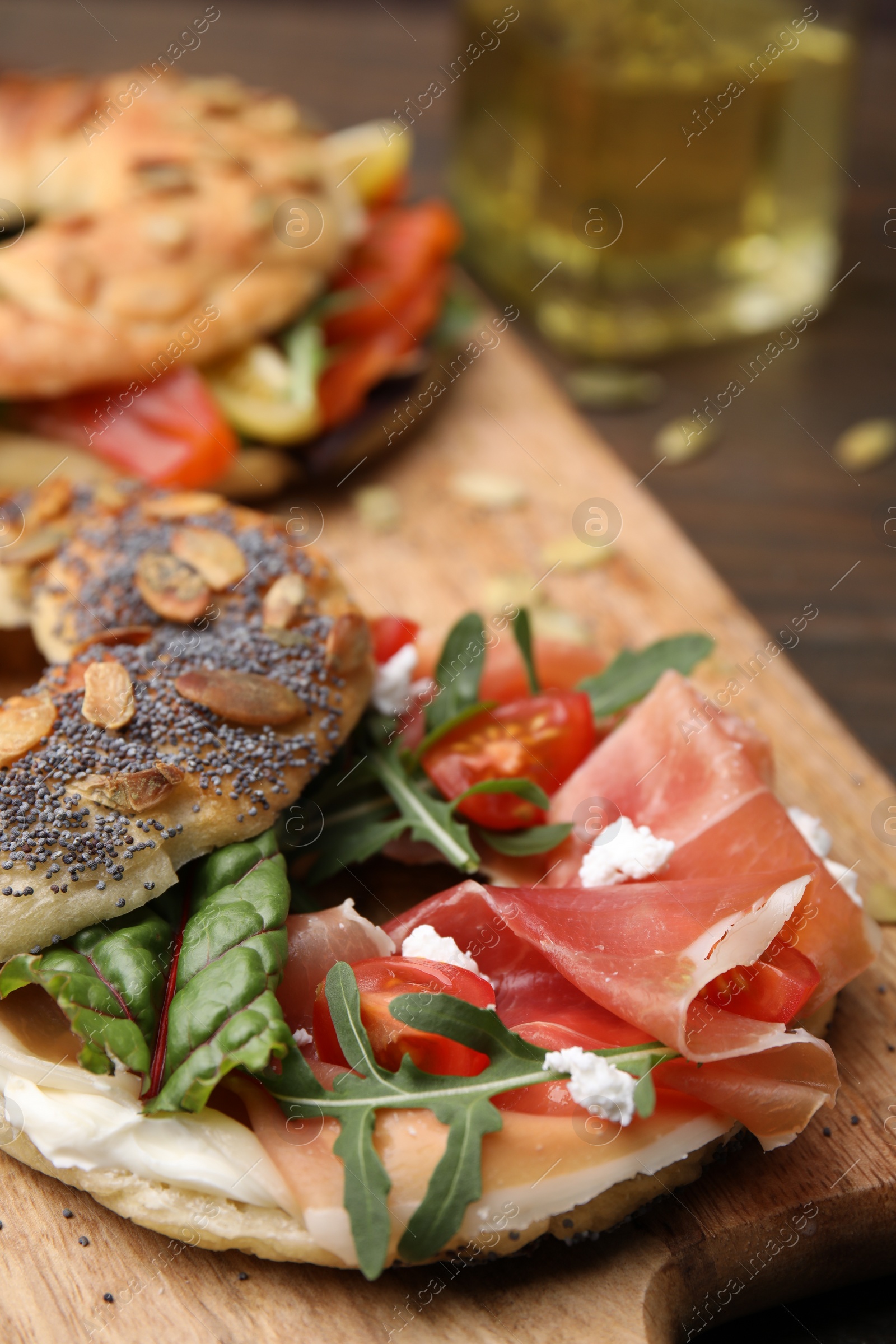 Photo of Tasty bagel with cured ham, cream cheese, tomatoes and arugula on wooden board, closeup