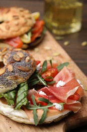 Photo of Tasty bagel with cured ham, cream cheese, tomatoes and arugula on wooden board, closeup