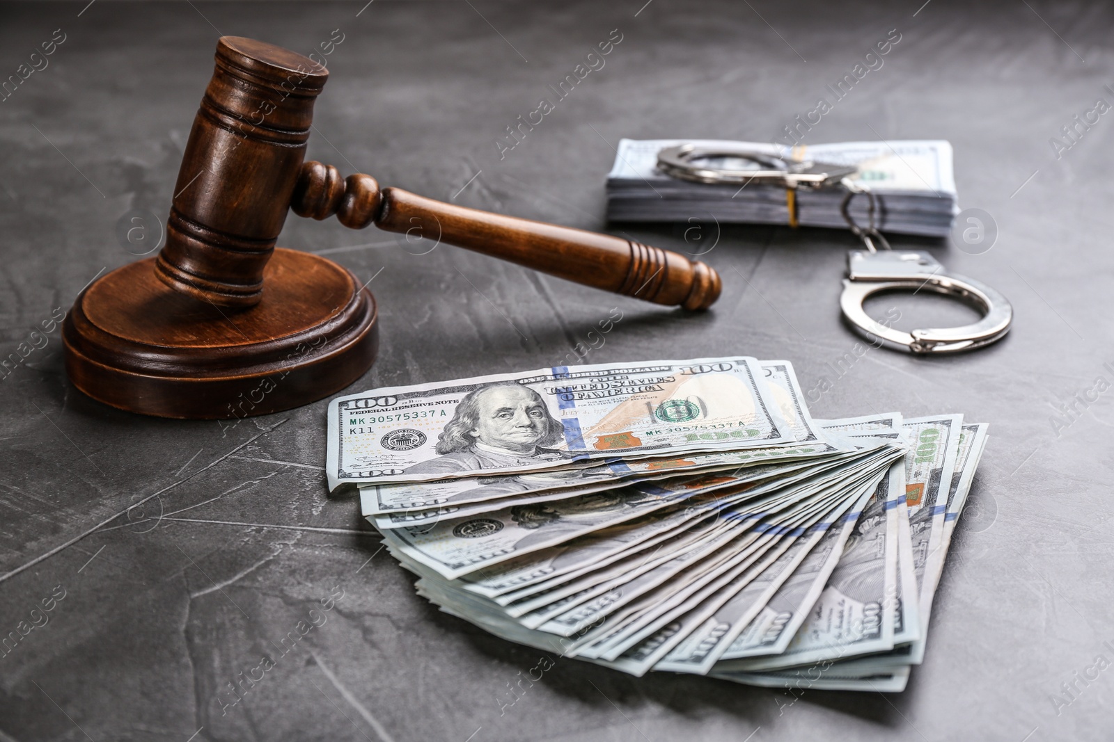 Photo of Dollar bills, handcuffs and gavel on grey stone table. Bribe concept