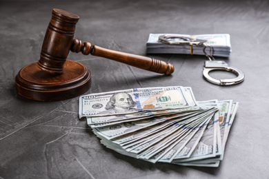 Photo of Dollar bills, handcuffs and gavel on grey stone table. Bribe concept