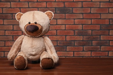 Photo of Cute teddy bear on wooden table near brick wall, space for text