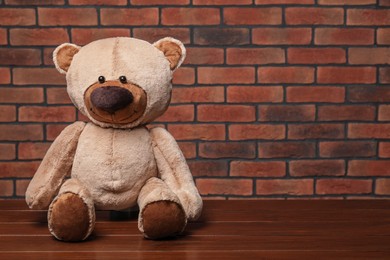 Cute teddy bear on wooden table near brick wall, space for text