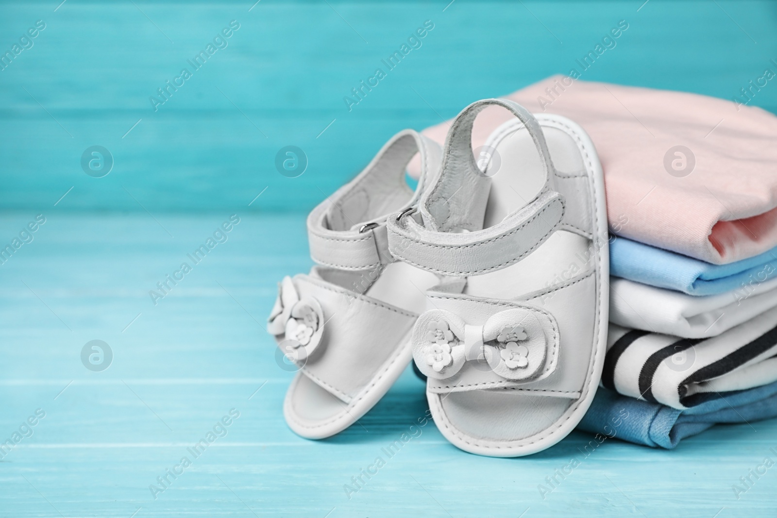 Photo of Pair of cute baby sandals and stack of clothes on table