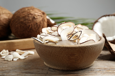 Tasty coconut chips in bowl on wooden table