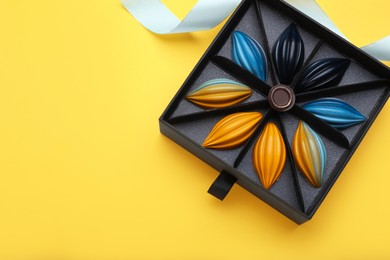 Photo of Box of tasty chocolate candies and ribbon on yellow background, flat lay. Space for text