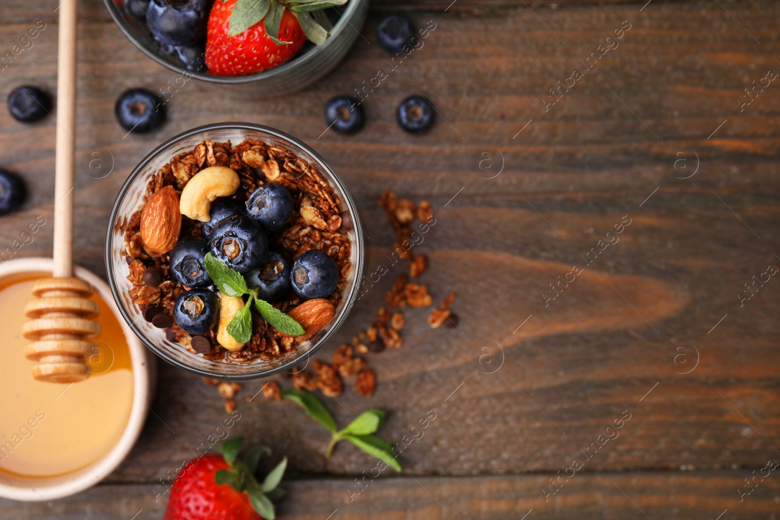 Photo of Tasty granola, berries, nuts and honey on wooden table, flat lay. Space for text