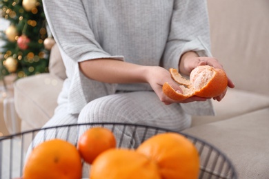 Photo of Woman peeling tangerine in room decorated for Christmas, closeup