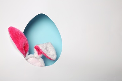 Photo of View of furry Easter bunny ears on color background through egg shaped hole, space for text