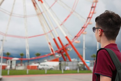 Photo of Teenage boy near large Ferris wheel outdoors. Space for text