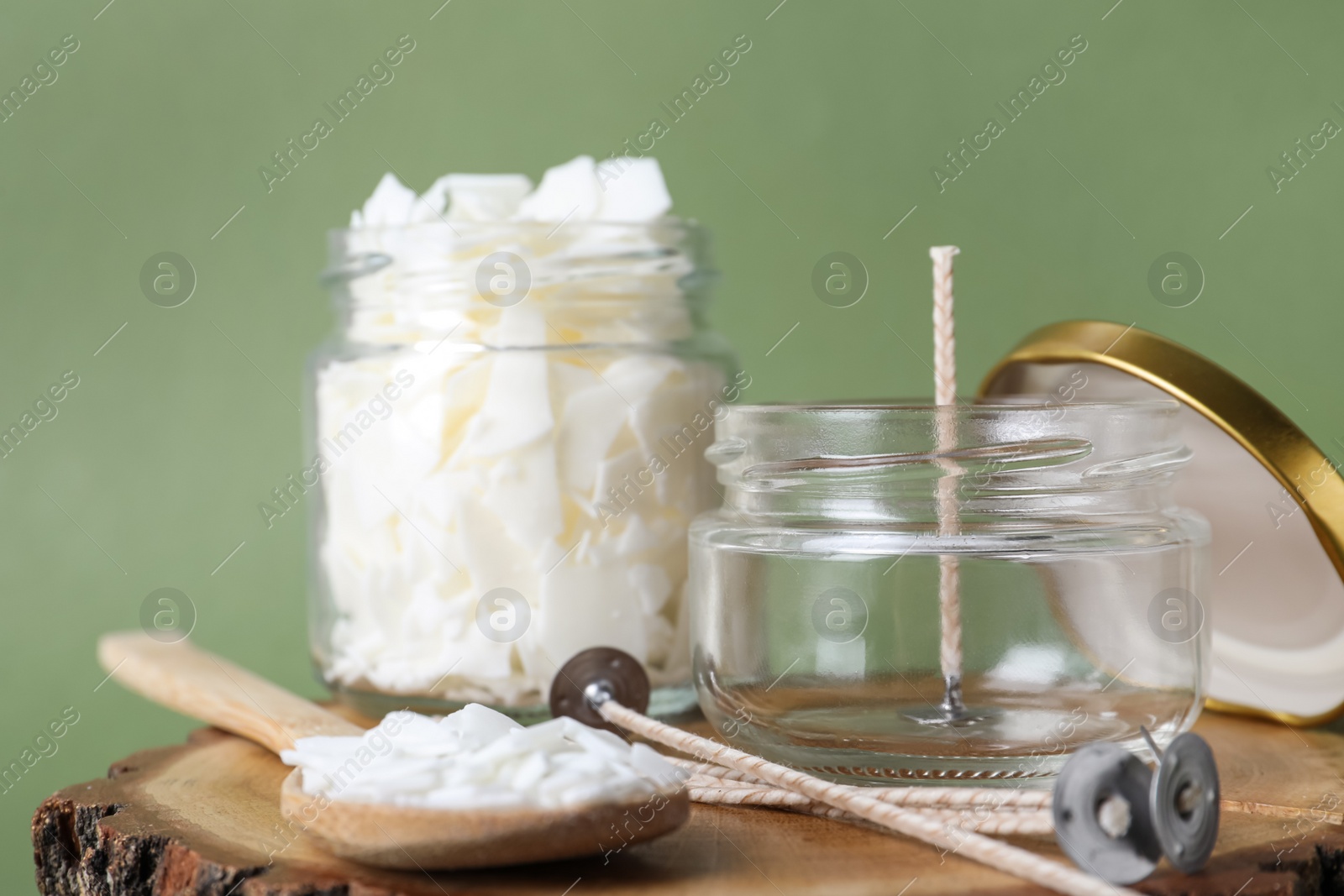 Photo of Ingredients for homemade candle on wooden stump against green background, closeup