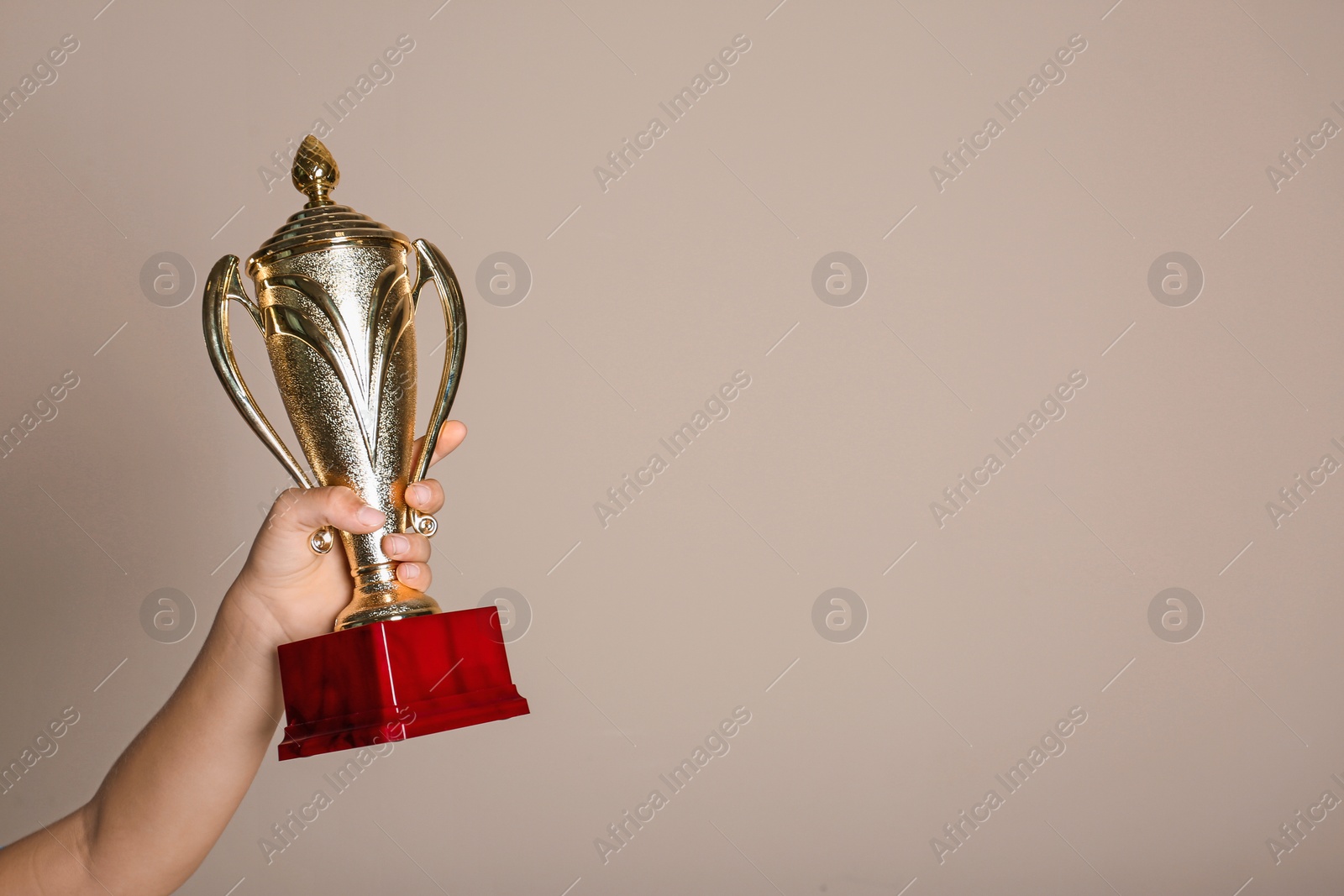 Photo of Child holding golden winning cup on beige background, closeup. Space for text