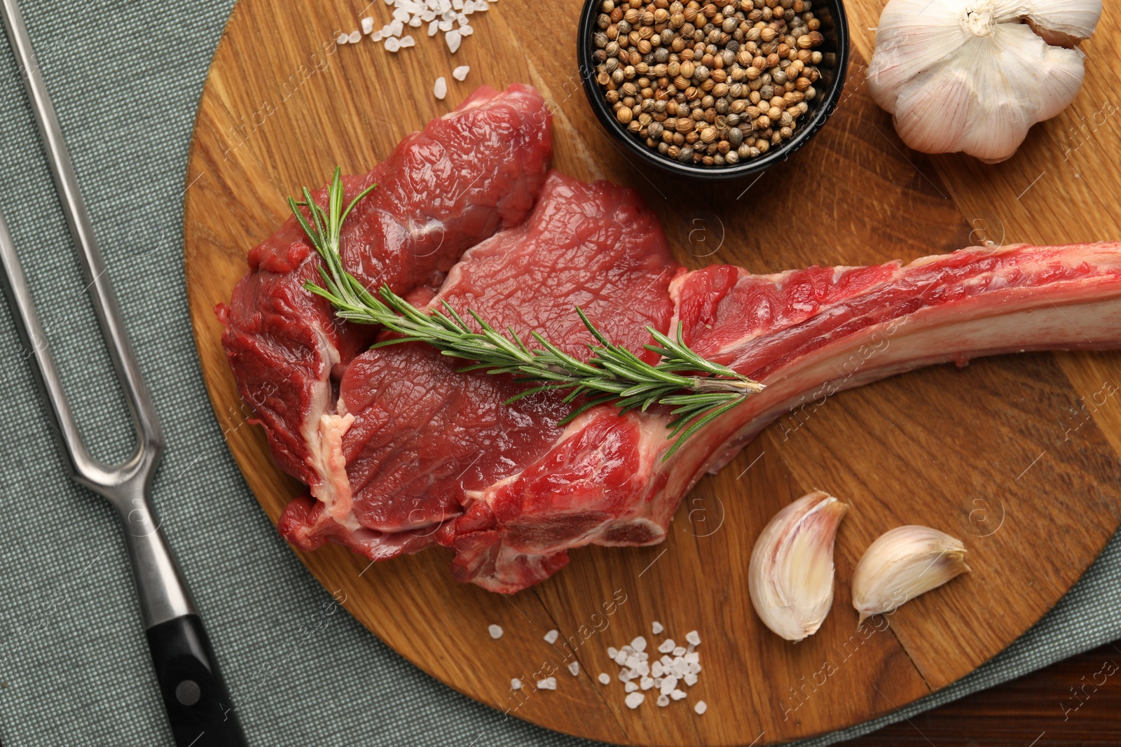 Photo of Raw ribeye steak, spices and fork on table, flat lay