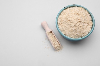 Photo of Scoop and bowl of brewer`s yeast flakes on light grey background, top view. Space for text