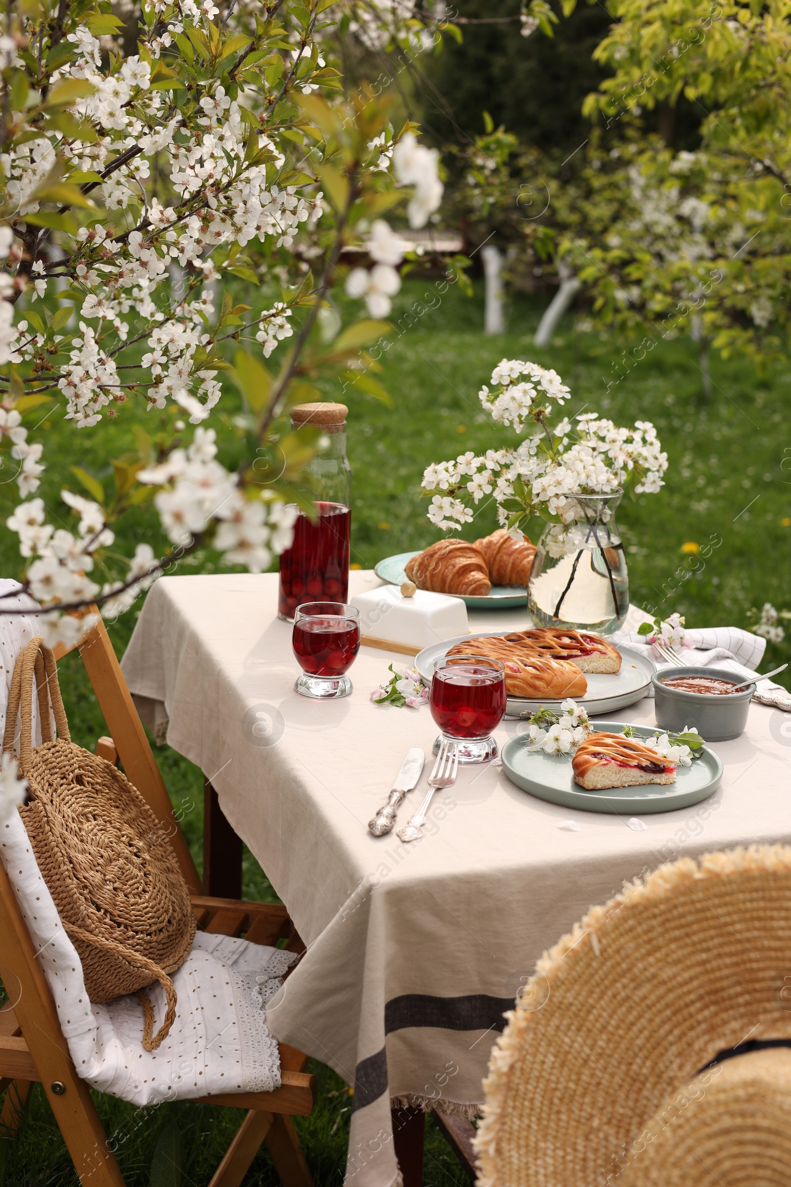 Photo of Stylish table setting with beautiful spring flowers, fruit drink and pie in garden