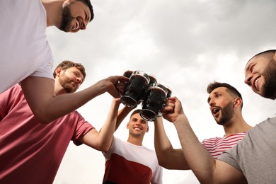 Friends clinking glasses with beer outdoors, low angle view