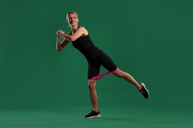 Photo of Smiling woman exercising with elastic resistance band on green background