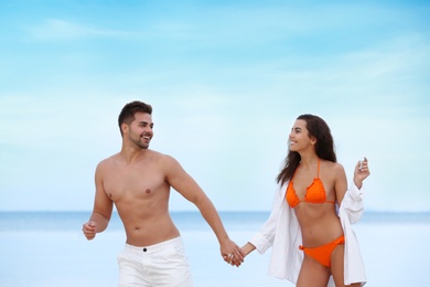 Happy young couple walking together on beach near sea