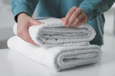 Woman touching soft white towel indoors, closeup