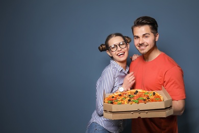 Attractive young couple with delicious pizza on color background