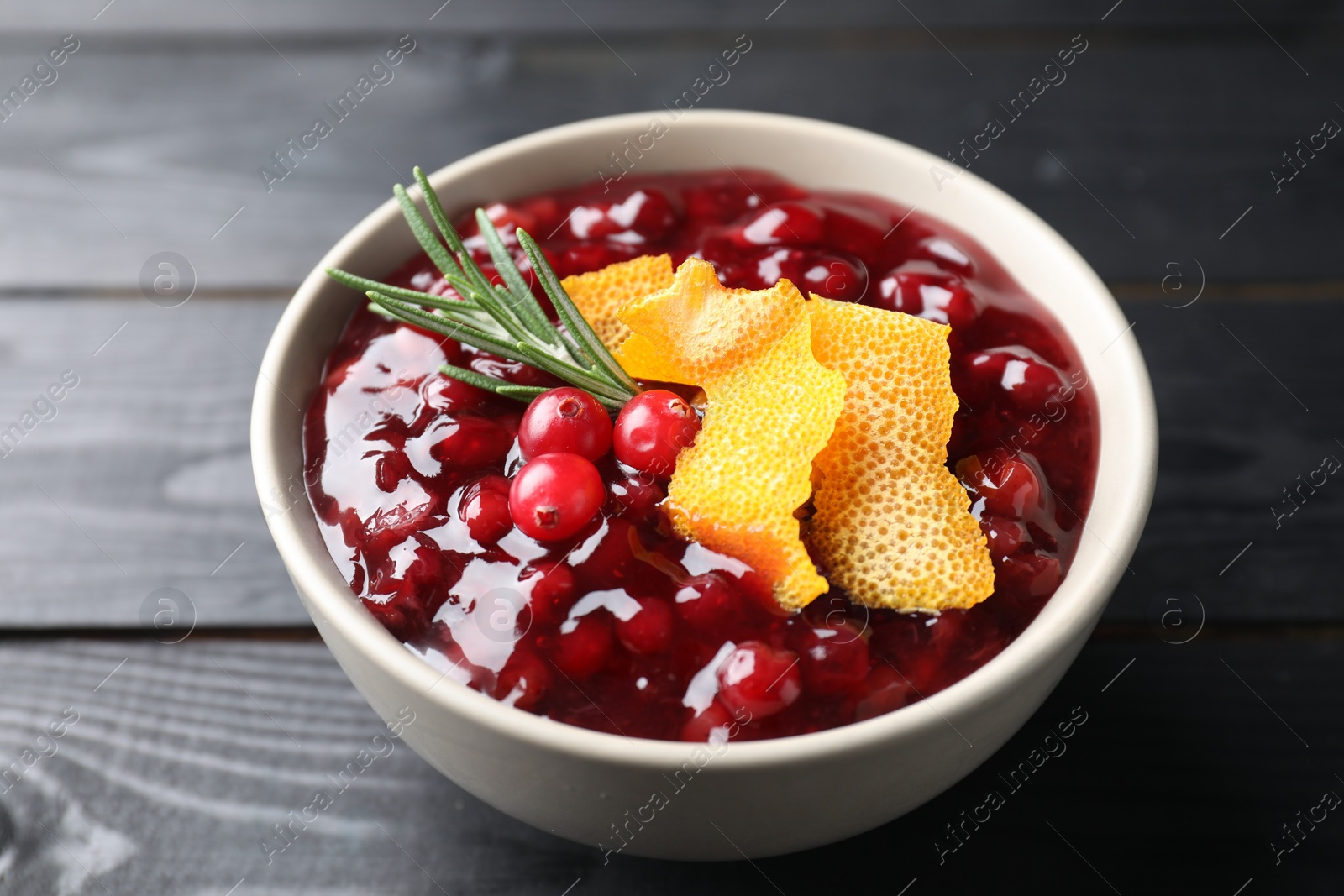 Photo of Fresh cranberry sauce, rosemary and orange peel in bowl on black wooden table, closeup