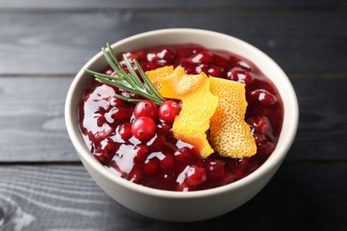 Fresh cranberry sauce, rosemary and orange peel in bowl on black wooden table, closeup