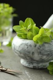 Photo of Mortar with sprigs of fresh green oregano and scissors on gray table, closeup