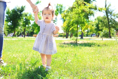 Photo of Adorable baby girl holding mother's hand while learning to walk outdoors