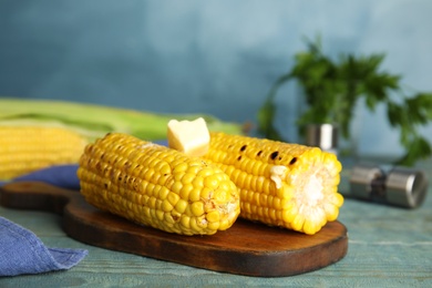 Fresh grilled corn cobs with butter on blue wooden table, closeup