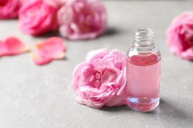 Photo of Bottle of rose essential oil and fresh flowers on table, space for text