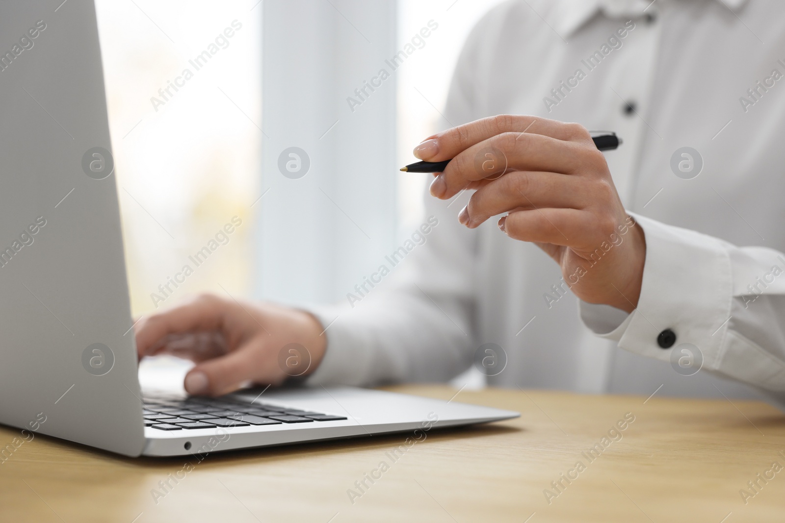 Photo of Woman with pen working on laptop at wooden table, closeup. Electronic document management