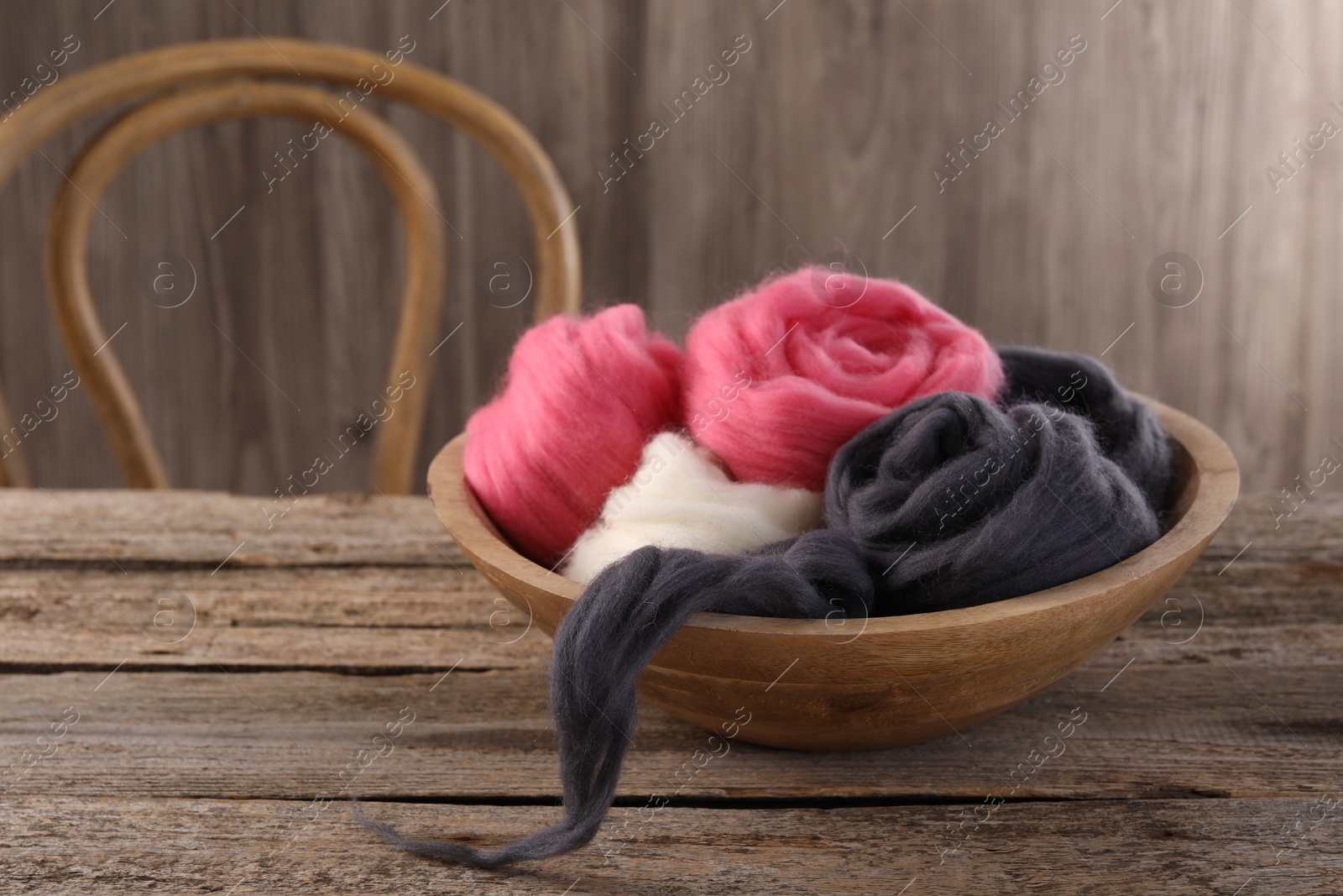 Photo of Colorful felting wool in bowl on wooden table, space for text