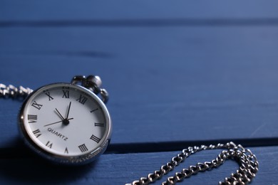 Photo of Silver pocket clock with chain on blue wooden table, closeup. Space for text