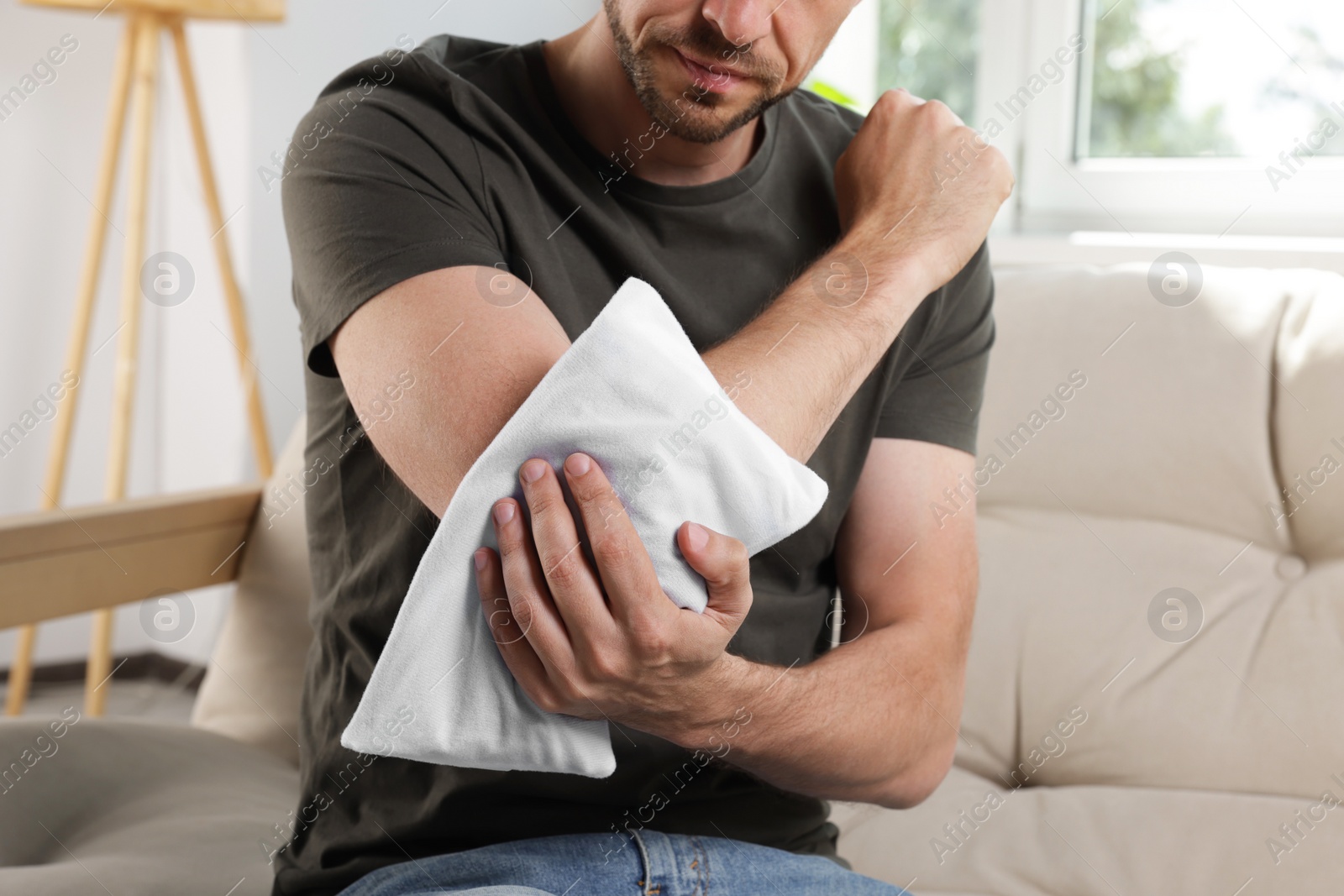 Photo of Man using heating pad on sofa at home, closeup