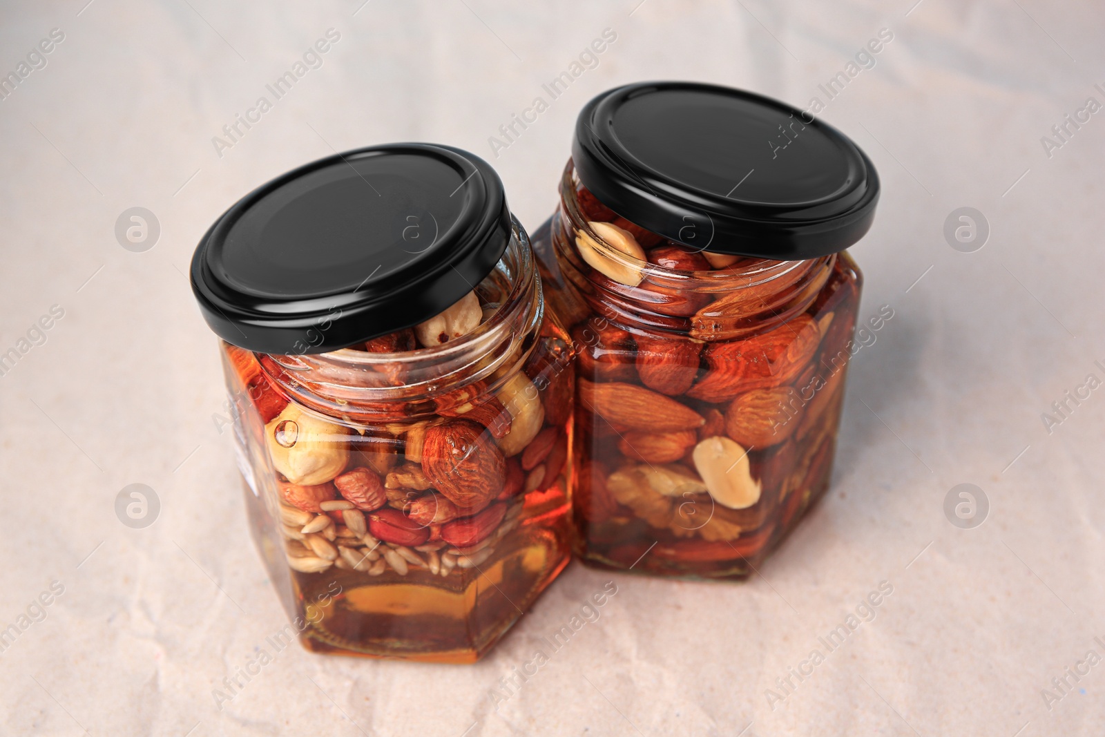 Photo of Jars with different nuts and honey on beige background