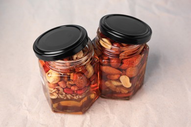 Photo of Jars with different nuts and honey on beige background