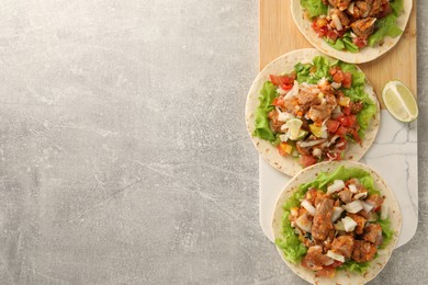 Delicious tacos with vegetables, meat and lime on grey textured table, top view. Space for text