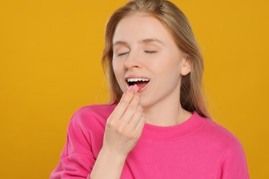 Happy young woman putting chewing gum into mouth on yellow background