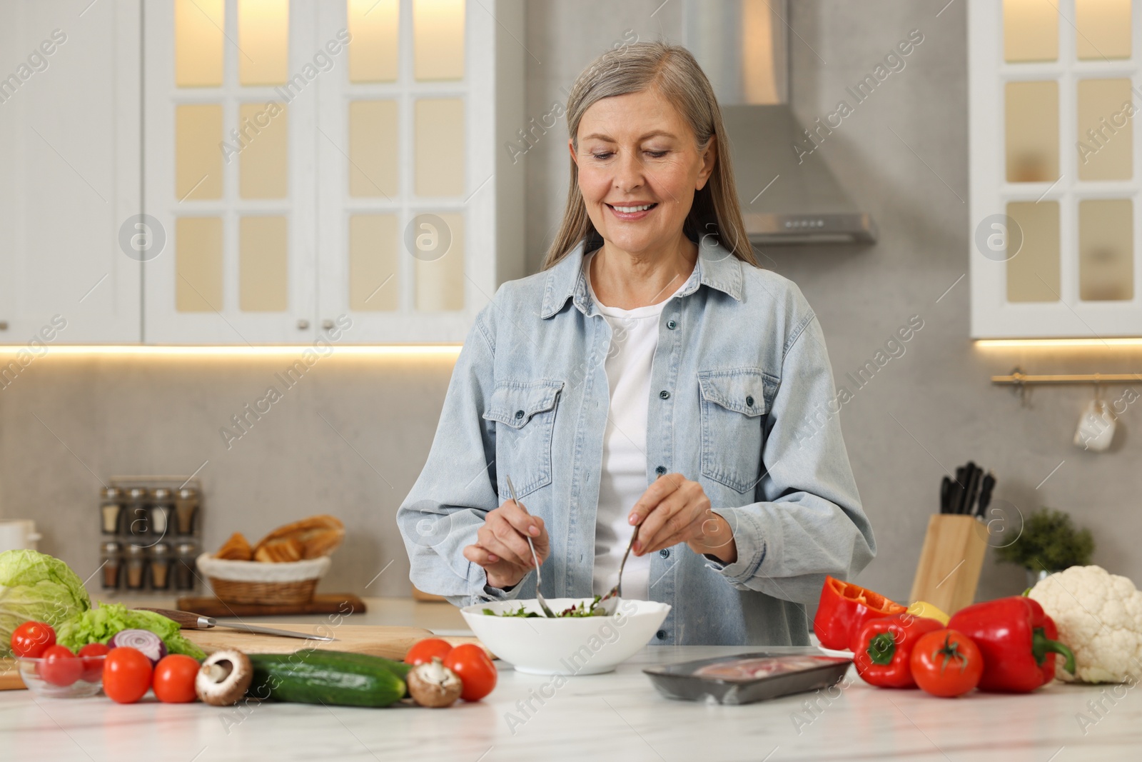 Photo of Happy woman making salad at table in kitchen