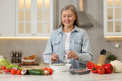 Photo of Happy woman making salad at table in kitchen