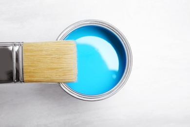 Photo of Can with blue paint and brush on light background, top view