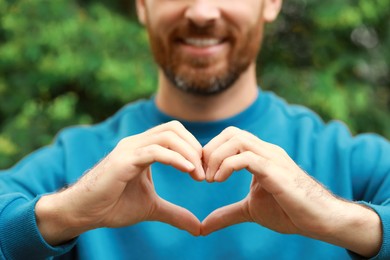 Photo of Happy man making heart with hands outdoors, closeup