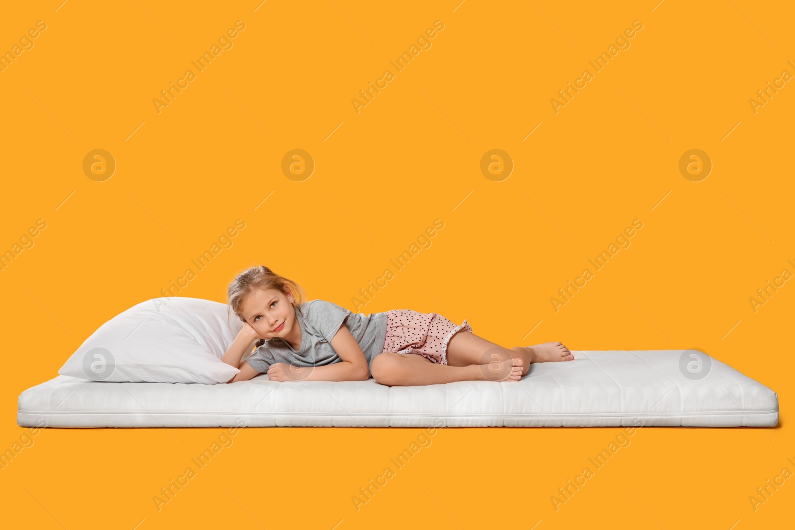 Photo of Little girl lying on comfortable mattress against orange background, space for text
